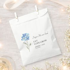 a white bag with blue flowers on it next to some wine glasses and baby's breath