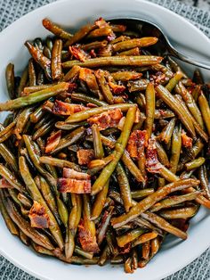 a white bowl filled with green beans and bacon on top of a blue table cloth