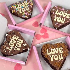 four heart shaped cookies with chocolate frosting and sprinkles in pink boxes