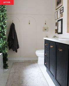 a white toilet sitting next to a black cabinet in a bathroom with pictures on the wall