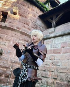 a woman dressed in costume standing next to a brick building with chains on her hands