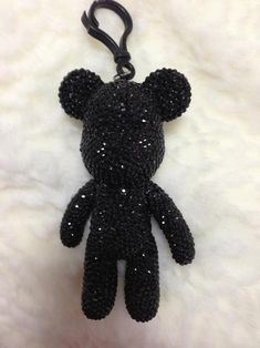 a black teddy bear keychain hanging on a white fur surface