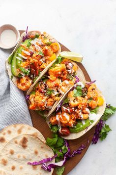 three tacos with chicken and vegetables on a wooden plate next to a bowl of ranch dressing