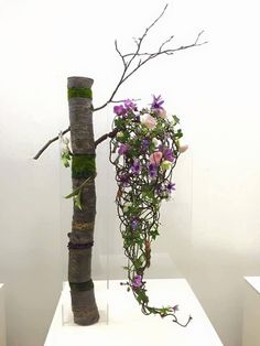 a vase with flowers and branches on display in a white walled room next to a tree