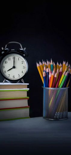 an alarm clock sitting on top of a stack of books next to a cup filled with pencils