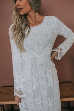 a woman standing in front of a table wearing a white dress with long sleeves and lace detailing