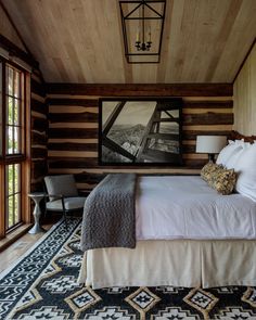 a bedroom with wood paneling and white bedding in the center is decorated with an area rug