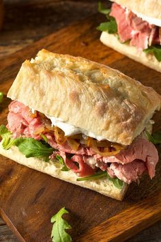 a sandwich with meat, cheese and lettuce on a cutting board next to another sandwich