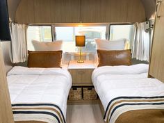 there are two beds in the inside of a camper with white sheets and brown pillows