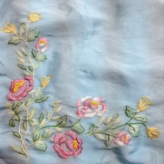 an embroidered blue fabric with pink flowers and leaves on the side, along with green stems