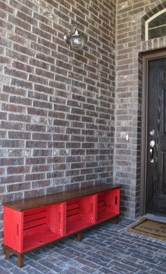 a red bench sitting in front of a brick wall next to a door with a sign on it