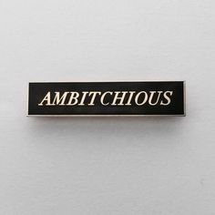 a black and white pin with the words ambitioushouse written on it's side