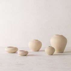 three white vases sitting next to each other on top of a table in front of a wall