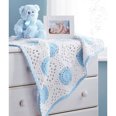 a blue teddy bear sitting on top of a dresser next to a crocheted blanket