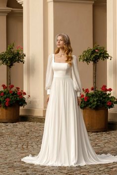 a woman in a white wedding dress standing on a cobblestone area with potted plants behind her