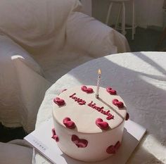 a birthday cake sitting on top of a table next to a white chair and pillows