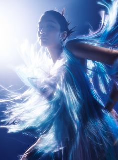 a woman with blue feathers on her body and hair blowing in the wind at night