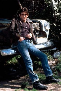 a man sitting on top of an old truck in front of some trees and bushes