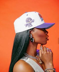 a woman with long black hair wearing a white hat and earring on an orange background