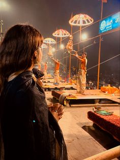 a woman standing in front of a stage with umbrellas on top of it at night