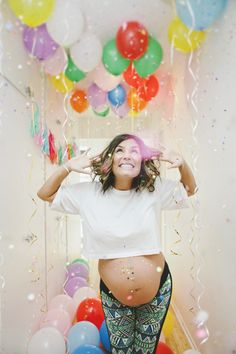 a pregnant woman standing in front of balloons and streamers with her hands behind her head