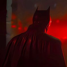 the dark knight is standing in front of a red light with his head turned to the side