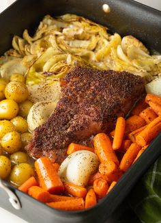 a pan filled with meat, potatoes and carrots on top of a green towel