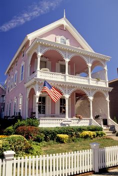 a large pink house with an american flag on the front porch and white picket fence