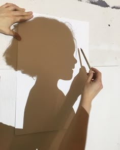 the shadow of a person holding a pair of scissors next to a piece of paper