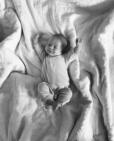 a black and white photo of a baby laying on a bed covered in sheets with his arms stretched out