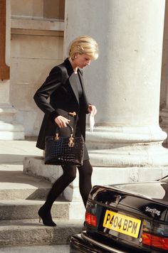 the woman is walking down the street with her hand on her hip and carrying a black purse