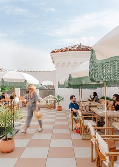 people sitting at tables with umbrellas and plants on the roof top terrace, while one person walks past them