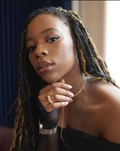 a woman with dreadlocks wearing a black top and holding her hand on her chin