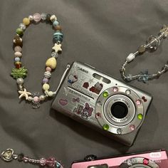 a camera and some beads are laying on a bed next to each other, including a necklace