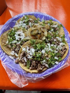 three tacos with meat, onions and herbs on a purple plate sitting on an orange table