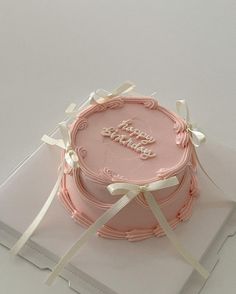 a pink birthday cake sitting on top of a white box with ribbon around the edges