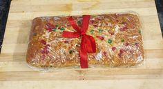 a loaf of bread wrapped in plastic and tied with a red ribbon on a cutting board