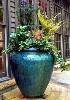 a large blue vase with plants in it on the ground next to a building and windows