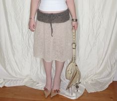 a woman standing in front of a white curtain wearing a skirt and holding a purse