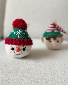 two small crocheted snowmen sitting next to each other on a white surface