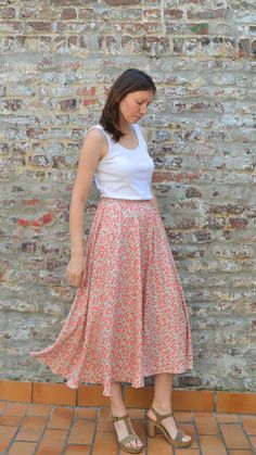 a woman standing in front of a brick wall wearing a white top and floral print skirt