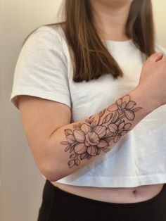 a woman wearing a white t - shirt and holding her arm with flowers on it