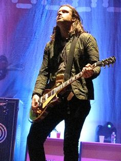 a man with long hair playing guitar on stage