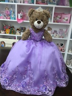 a teddy bear dressed in a purple dress sitting on a table next to shelves full of toys