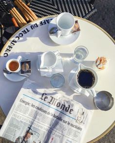 two cups of coffee are sitting on a table with newspaper and utensils next to it