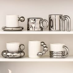 some coffee cups and mugs are sitting on the white shelves in front of each other