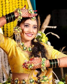 a woman in a yellow sari is holding her hands up to her head and smiling