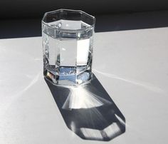 a clear glass sitting on top of a white table next to a shadow from the sun