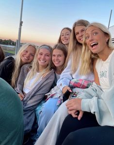 a group of young women sitting next to each other on top of a boat at sunset