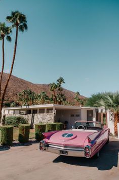 a pink car parked in front of a palm tree lined driveway with a house behind it